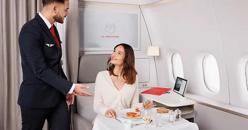 Service gastronomique à bord de la cabine La Première d’Air France avec hôtesse et repas dressé à table