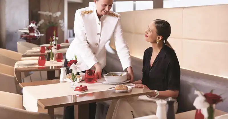 Service en table au restaurant du salon La Première d’Air France avec hôtesse servant un plat chaud à une cliente